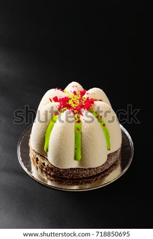 Mini mousse pastry dessert covered with white chocolate velour and decorated with green glaze and red crumbs on black background. Modern european cake. French cuisine