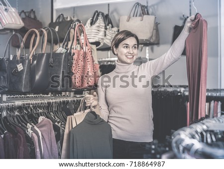 Young positive female shopper examining turtleneck sweaters in women`s cloths shop