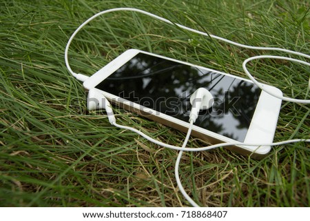Smartphone and headphones lying on a background of green grass, break.