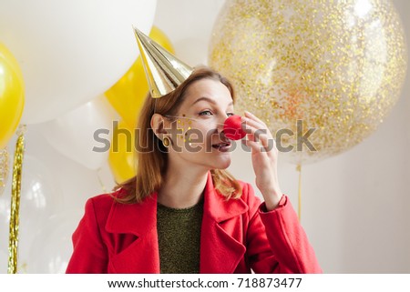 Young woman in a celebratory cap fooling around at a party on the background of falling confetti