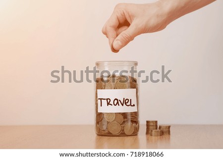 Distribution of cash savings concept. Hand puts coins to the glass money boxes with inscription 'travel'