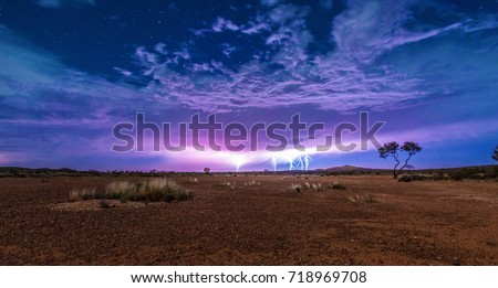 Five lightnings on a cloudy sky full of stars with the red dry soil of the outback desert under it. Thunderstorm lightning. Royalty-Free Stock Photo #718969708
