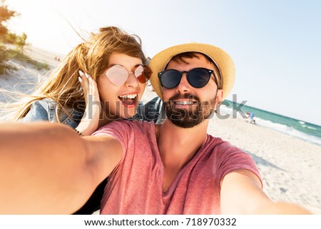 Positive fun self portrait of  young  traveling couple in love , best friends , having fun on  amazing tropical beach.   Attractive wonder girl with red  stylish hipster boyfriend enjoying holidays. 
