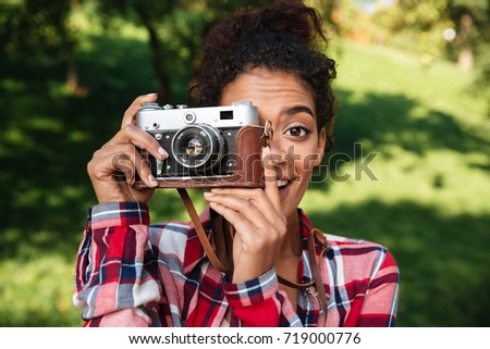 Picture of amazing young african woman photographer sitting outdoors in park. Holding camera.