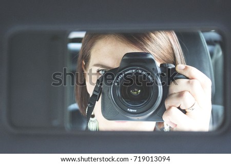 Young girl woman holding a digital camera taking picture of herself looking into the small mirror of car. Self shoot indoor. portrait of photographer in car with photo camera. Black background.