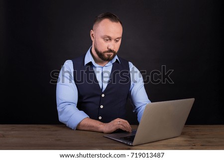 Closeup view of a bearded young businessman working at the office. Man using a laptop. Portrait of young man sitting at his desk in the office. Black background
