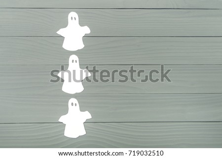 Left side of paper silhouette of three white ghosts on grey wooden background. Halloween holiday background. Copy space