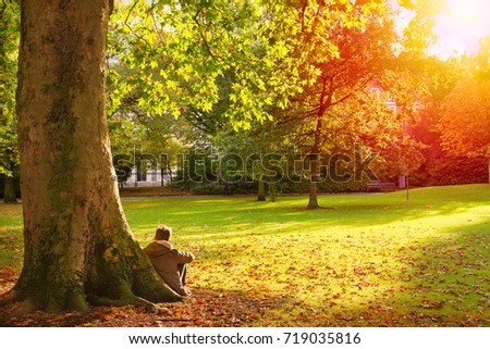 Man in autumn park. Guy resting on park lawn, autumn. Boy outdoor, horizontal