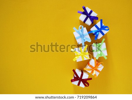Many festive boxes. Gift in the box. Multicolored ribbons. Boxes in a row. Rainbow. Happiness. New Year. Christmas. Birthday. Celebration. Yellow background.