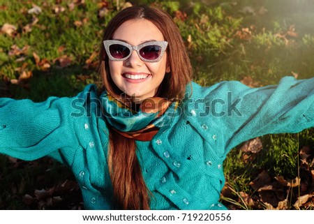 Portrait of a smiling young girl making selfie photo in park.Young girl takes a selfie on the backgroung of a wall with autumn beautiful leaves.