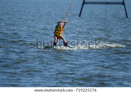 Wake Park. Children learn to kite, slide on water on board for Kite-boarding. Summer water sports. Little boy is learning new fashionable extreme sport - Kite-surfing, Wake-boarding