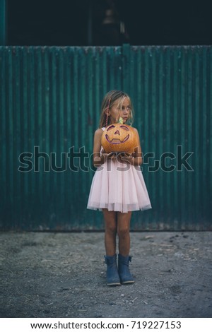 Blond girl with blue eyes holding a pumpkin halloween on green door