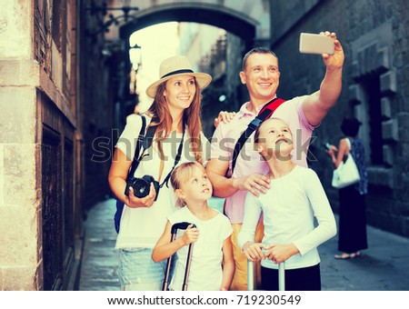 Cheerful travelers family of four walking on city streets and making selfie