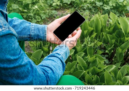  Mobile phone in hands a young hipster business man in denim shirt and green jeans on the background of green grass with paving stone