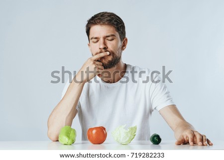 a vegan man with a beard looks at vegetables on a light background, vegetarianism                               