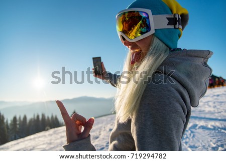Female snowboarder enjoying sunset after snowboarding, using her smart phone, taking pictures of winter nature in the mountains copyspace connectivity mobility freeride lifestyle concept