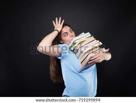 Woman student with a desperate look carrying many books on dark background