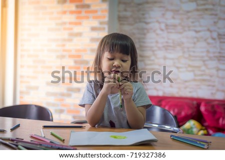 Asian girl is practice painting picture with crayon color on the table.