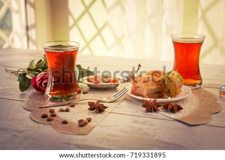 Two traditional glasses of Turkish tea and lukum in lukumluk and plate with baklava decorative flowers and badyan on a sunny day on a wooden table vintage toned picture close-up shallow depth of field