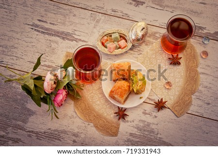 Two traditional glasses of Turkish tea and lukum in lukumluk and plate with baklava decorative flowers and badyan on a sunny day on a wooden table vintage toned picture close-up shallow depth of field