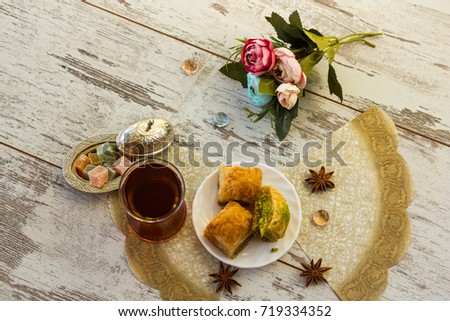 traditional glass of Turkish tea and lukum in lukumluk and plate with baklava decorative flowers and badyan on a sunny day on a wooden table vintage toned picture close-up shallow depth of field