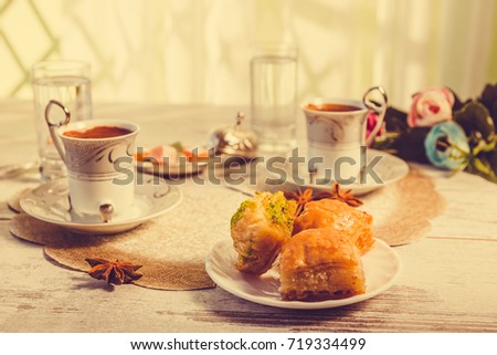 Two cups of Turkish coffee glasses of water and plate with baklava lukum in lukumluk decorative flowers and badyan on sunny day on wooden table vintage toned picture close-up shallow depth of field