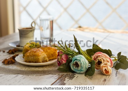 Cup of Turkish coffee and glasses of water and plate with baklava lukum in lukumluk decorative flowers and badyan on a sunny day on a wooden table vintage toned picture close-up shallow depth of field