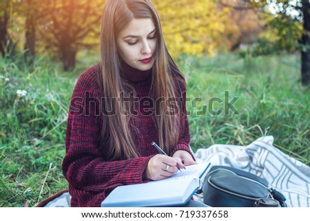 Beautiful woman writer writing with pen autumn story in her notebook. The concept of education and working with nature
