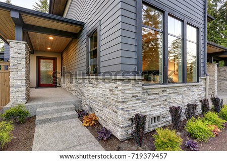 Luxurious new home with curb appeal. Trendy grey two-story exterior in Bellevue with large picture windows, stone siding, covered porch and concrete pathway. Northwest, USA Royalty-Free Stock Photo #719379457