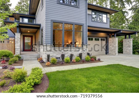 Luxurious new home with curb appeal. Trendy grey two-story exterior in Bellevue with large picture windows, stone foundation veneer, covered porch and concrete pathway. Northwest, USA