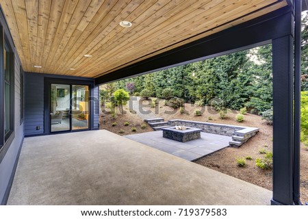 New modern home features a backyard with covered patio accented with a wood plank ceiling and a rectangular fire pit, made of concrete and slate tiles. Northwest, USA