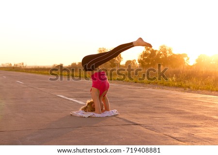Yoga professional performing pose and handstand. Peaceful healthy young girl doing power pose on rural backstage, road on sunset. Slim woman doing yoga over orange sun. 