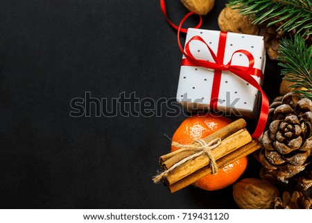 Christmas New Year Composition Greeting Card. Tangerine Cinnamon Sticks Pine Cones Fir Tree branches Gift Box with Curled Red Ribbon Nuts on Dark Background. Template Copy Space.