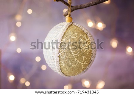 Linen and lace Christmas tree ball with ornament hanging on a branch. Golden garland glittering light in the background. Festive greeting card poster template. Copy space.