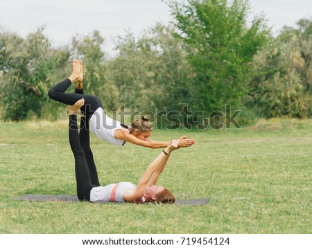 Girl in white shirt exercises yoga outdoor, on green grass. Blue sky on the background.