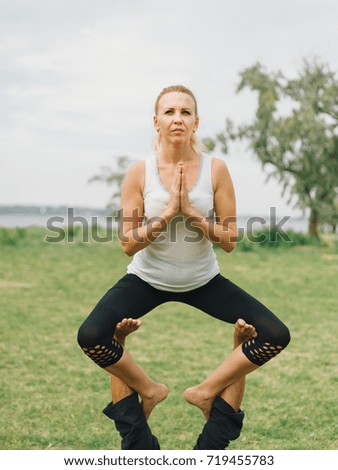 Girl in white shirt exercises yoga outdoor, on green grass.