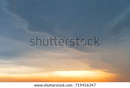 a orange sunset with a bright sun at the bottom of the photo with copy space left on top the blue gray clouds
