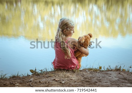 one caucasian girl with long blond hair sitting in the strand with teddy bear toy rear view