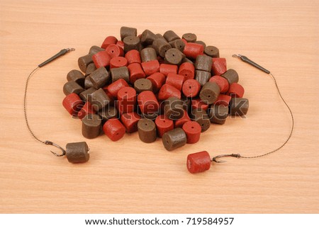 Fishing bait with hook and brown with red pre-drilled halibut pellets for carp fishing isolated on wood background with soft shadow
