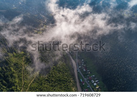 Beautiful nature landscape aerial view of the village in the Carpathian mountains with clouds in the foreground and sun rays. Top view. From above