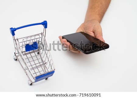 Hand holding a  smart phone and a  tiny shopping cart 