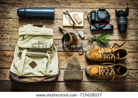 Traveling - packing (preparing) for adventure trip concept. Backpack, boots, hat, belt, thermos and camera on wooden background captured from above (flat lay).  Royalty-Free Stock Photo #719628037