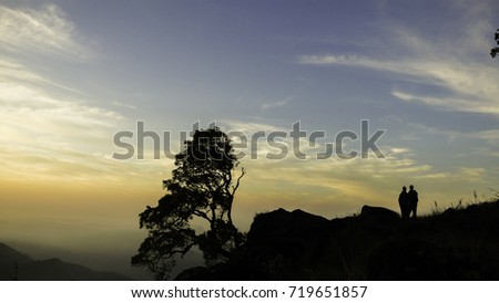 Silhouette of two people next to a tree on a cliff against the sunrise