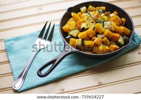 Colorful roasted rosemary butternut squash sweet potato and zucchini garnished with fresh rosemary in cast iron pan on blue fabric napkin on wood background
