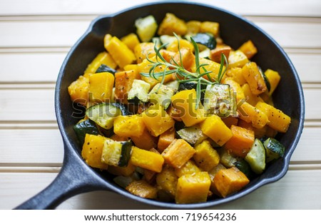Close up colorful roasted rosemary butternut squash sweet potato and zucchini garnished with fresh rosemary in cast iron pan on wood background 