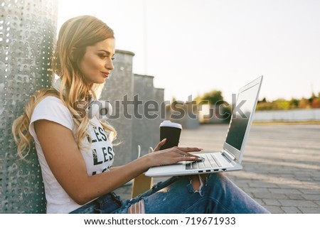 Young woman in white T-shirt with word "less" working for laptop and drinking coffee