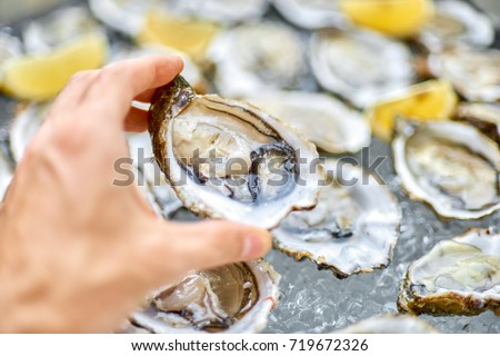 Open oyster in a man's hand, against a background of open oysters, close-up. Royalty-Free Stock Photo #719672326