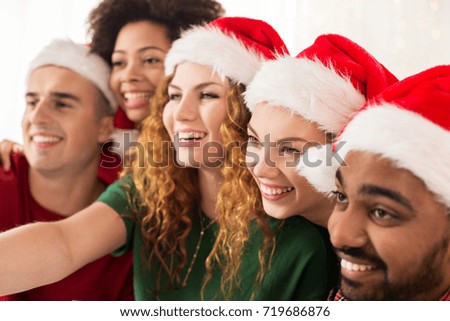 celebration and holidays concept - happy friends in santa hats taking selfie at christmas party