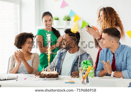 corporate, celebration and people concept - happy team with firework on birthday cake and non-alcoholic drinks greeting colleague at office party