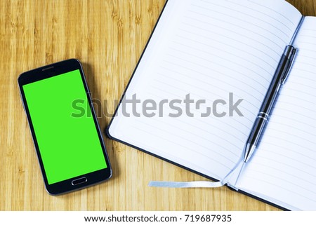 cell phone with green screen and notepad on wooden desk. smart phone concept background. copy space